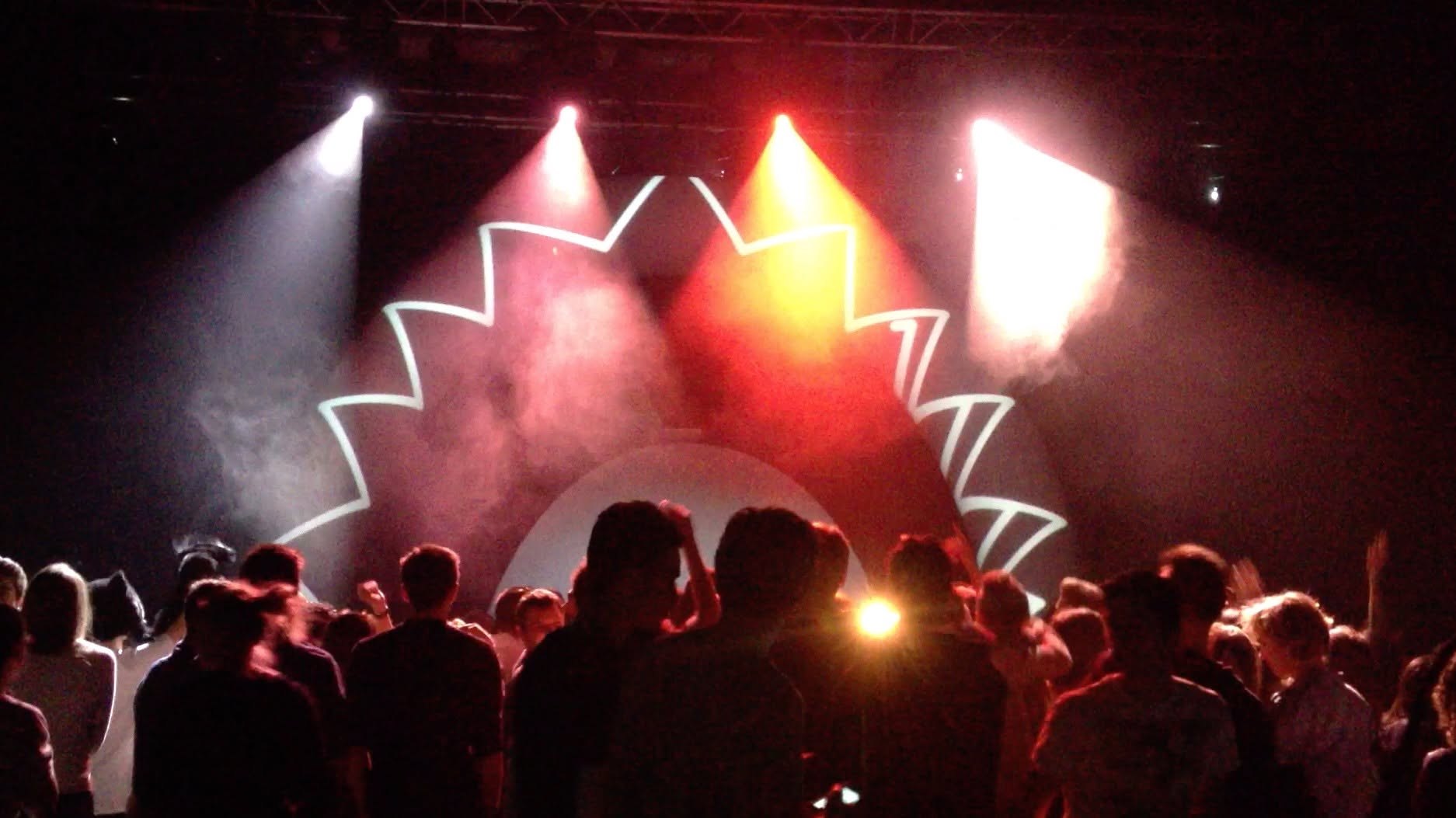 VJ live visuals on stage: white graphic projection with red and amber spotlights above the crowd