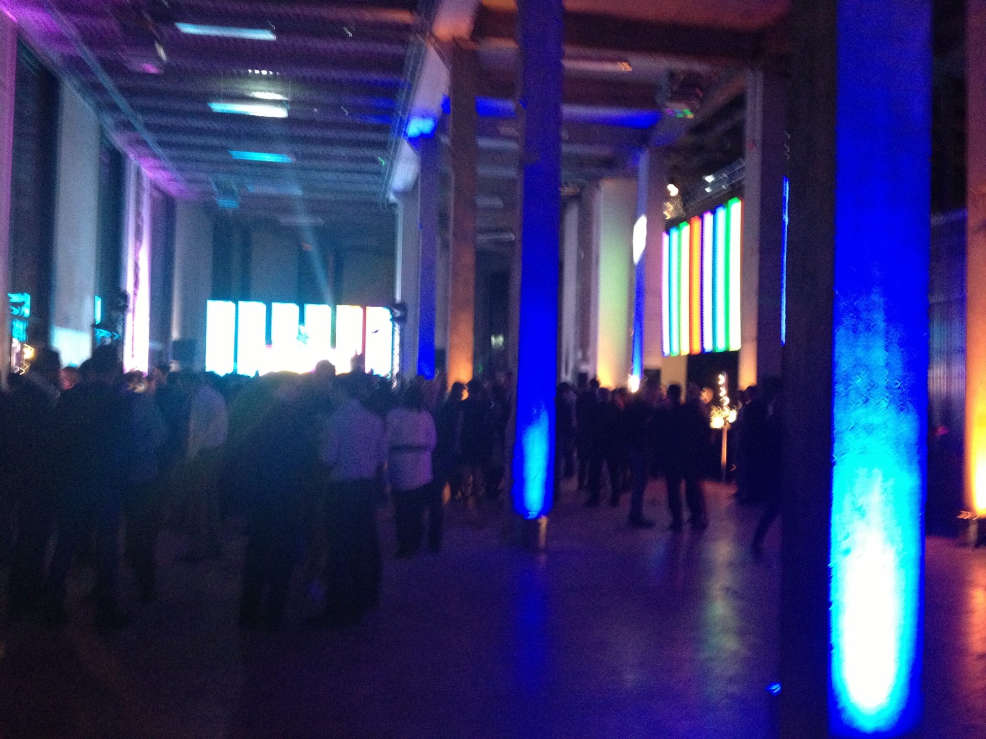 Large industrial hall with colored screens and blue light columns at an event