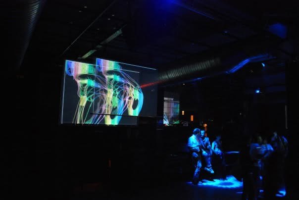 Projection mapping of colored line-drawn figures on a screen above a dance floor
