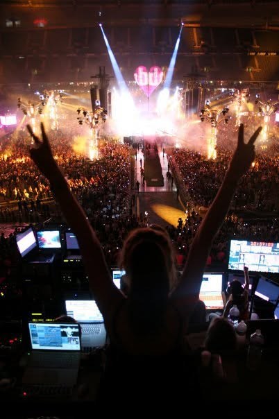VJ at the control desk with arms raised in front of a huge stage and crowd