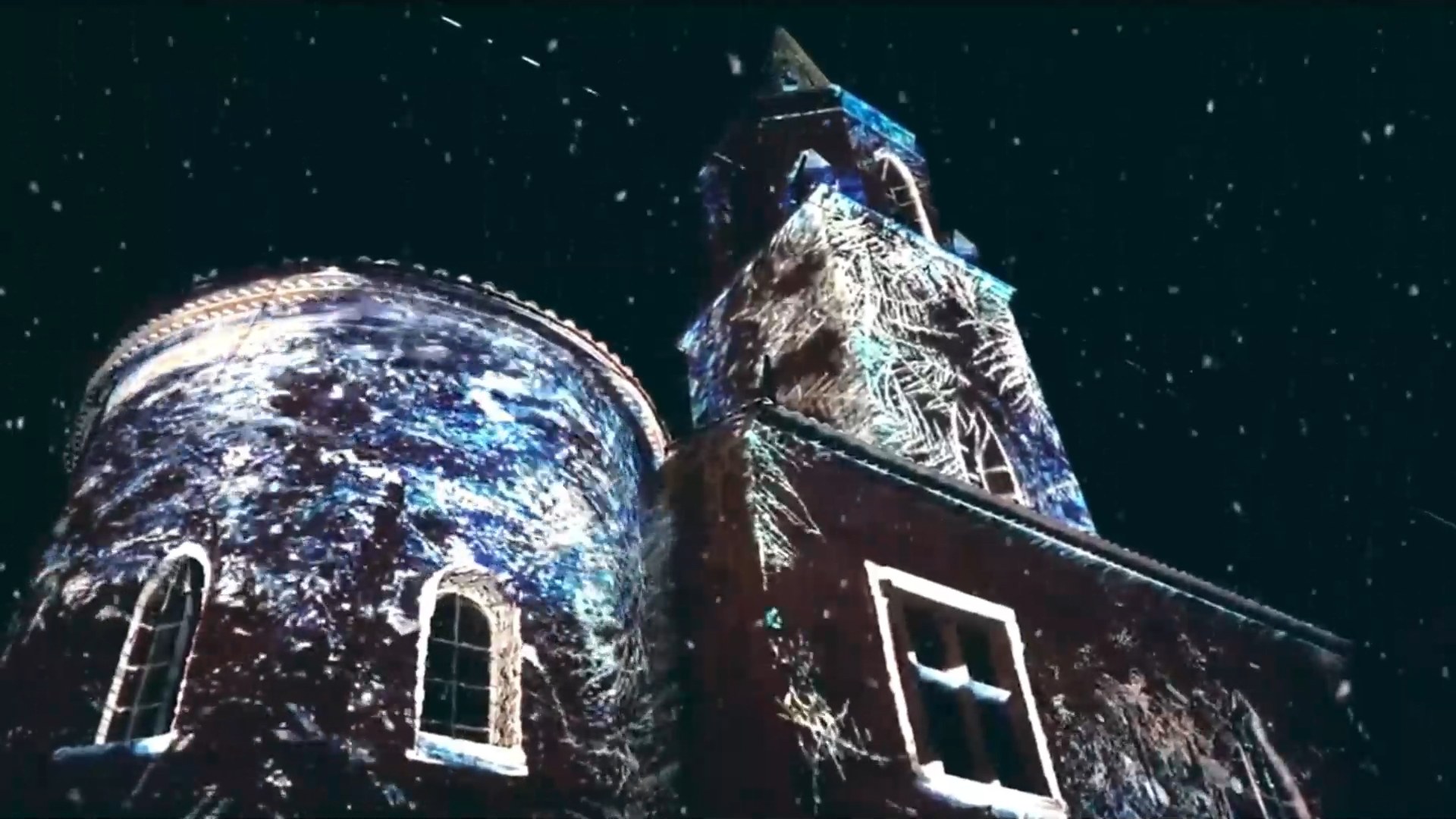 Architectural projection mapping on an old brick building and tower at night, with falling snow