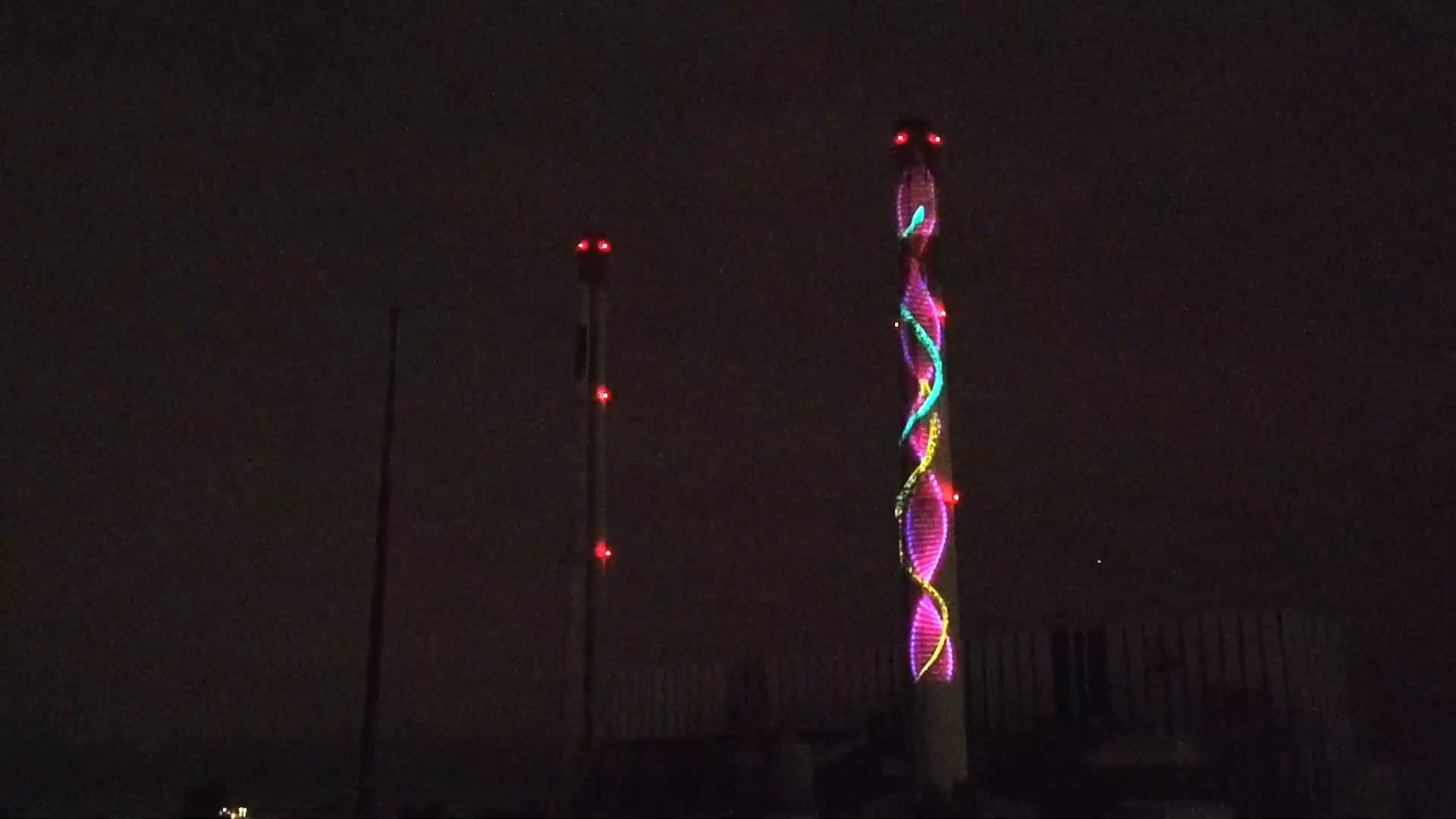 Projection mapping on an industrial chimney: a colorful helix of light climbing the tower at night