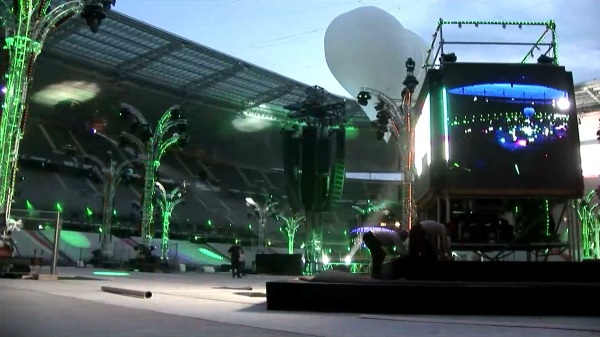 Stadium stage setup with green lit truss structures, a large white balloon and an LED screen